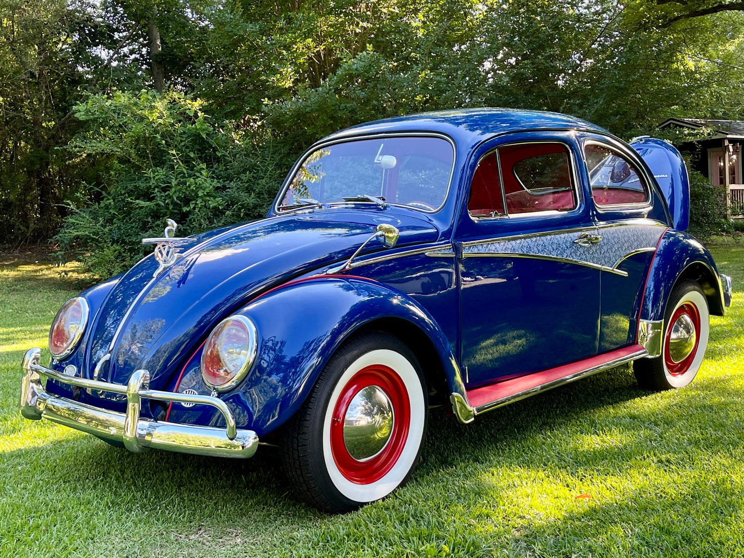 This image shows a classic Volkswagen Beetle in a deep blue color with red and white accents on the wheels. The car features chrome bumpers and detailed trim, along with a red interior visible through the windows.